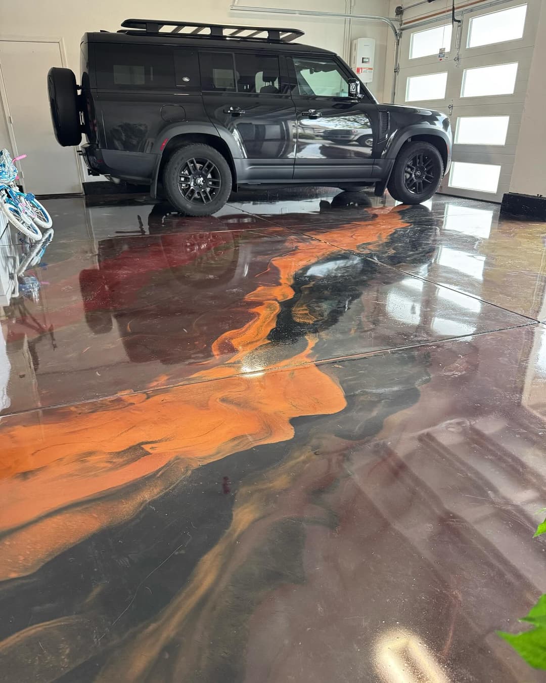 Black SUV parked on glossy epoxy floor with striking orange swirl design. Modern garage setting.