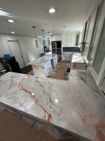 Modern kitchen with marble countertops, under construction, featuring bright lighting and cabinetry.