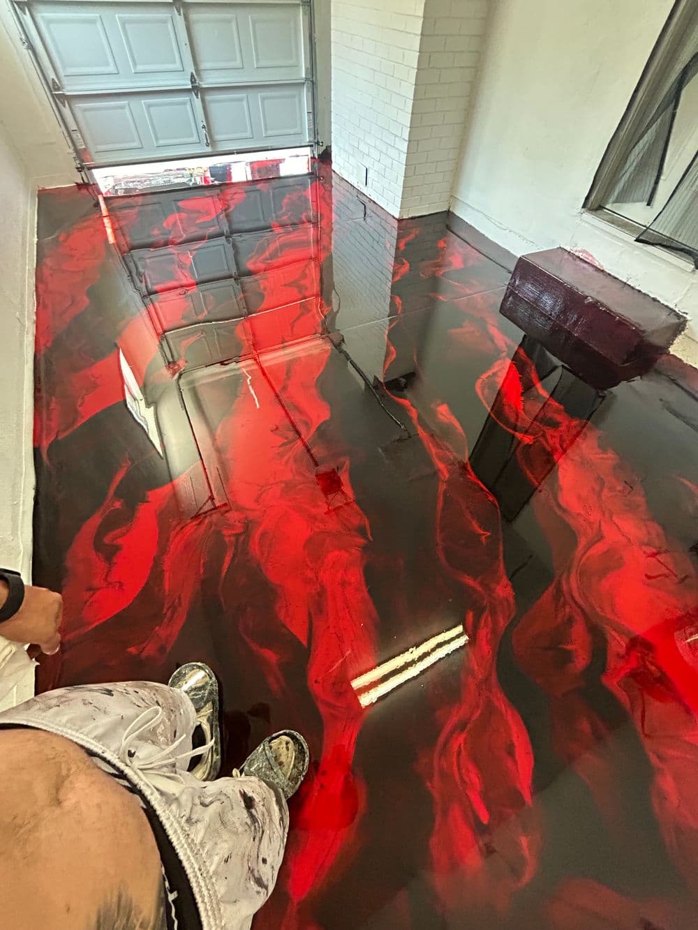 Epoxy resin floor with red and black swirls in a garage setting, reflecting light.