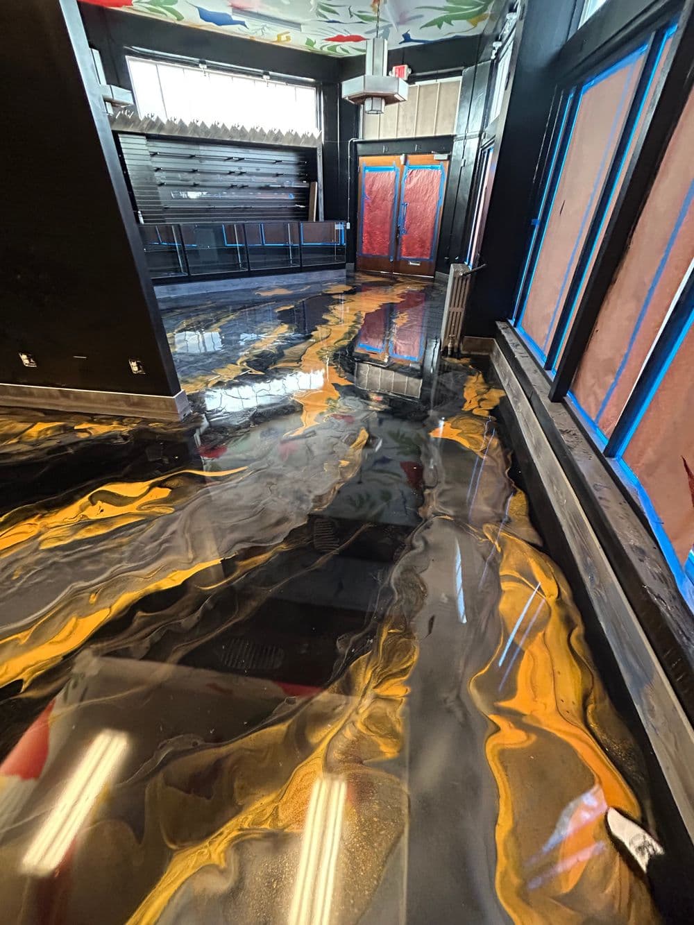 Colorful epoxy resin floor with black, gold, and orange swirls in a modern interior space.