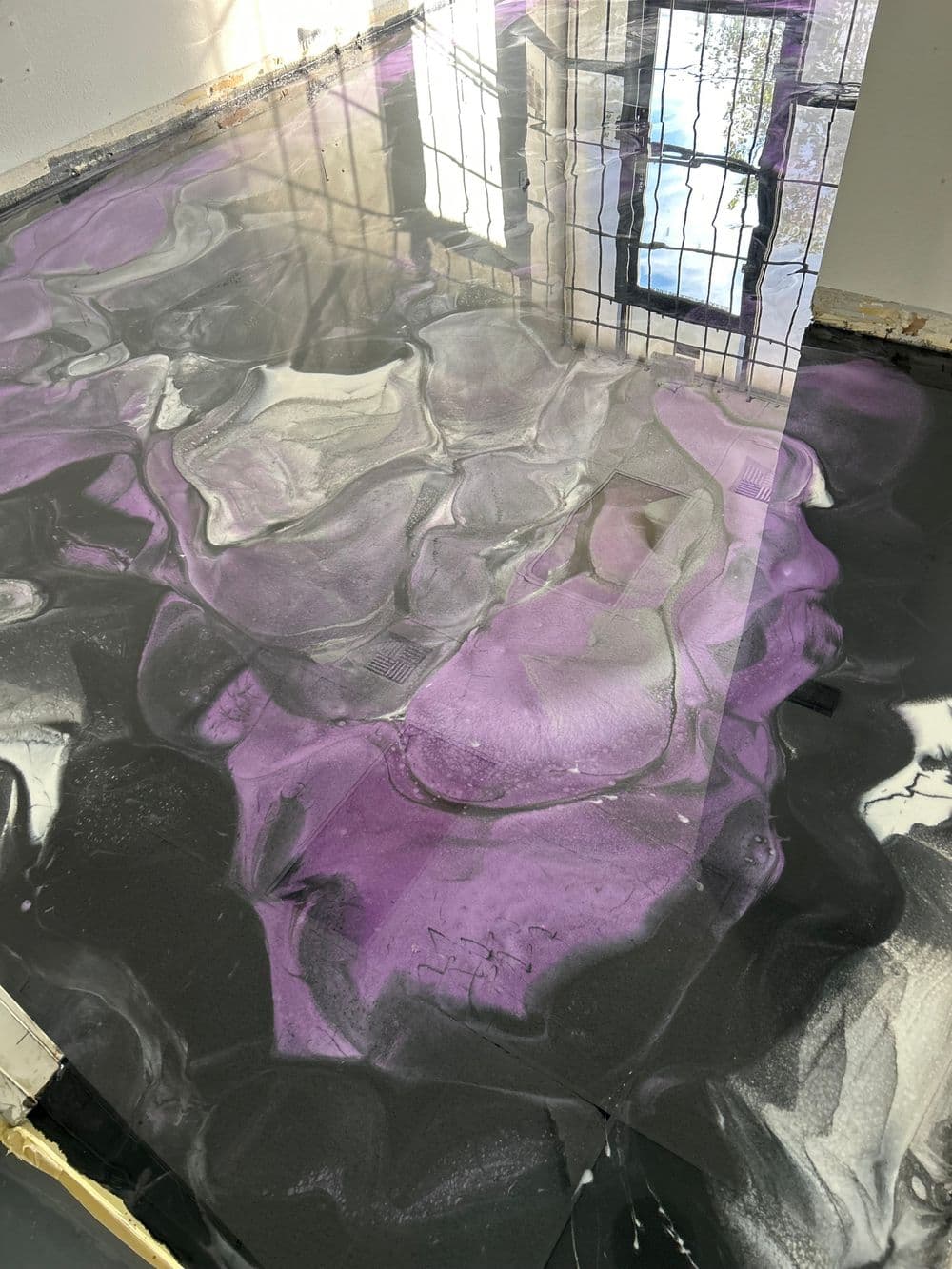 Abstract resin floor with swirls of purple, black, and gray, reflecting natural light.
