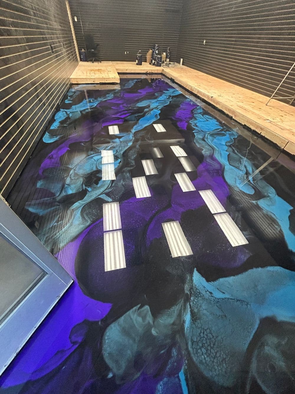 Artistic epoxy resin floor with abstract blue and purple swirls, illuminated by overhead lights.