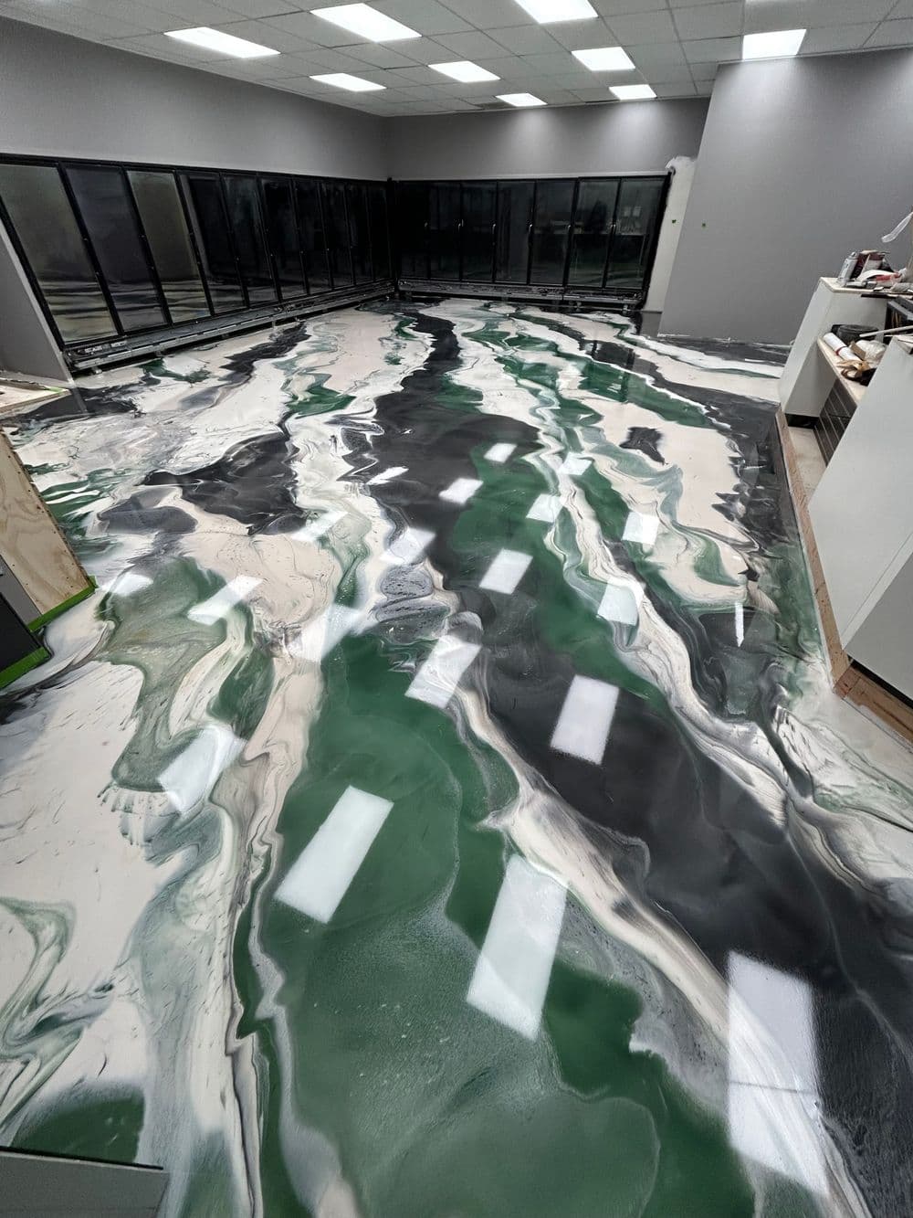 Epic epoxy floor design featuring green, black, and white swirling patterns in a spacious room.