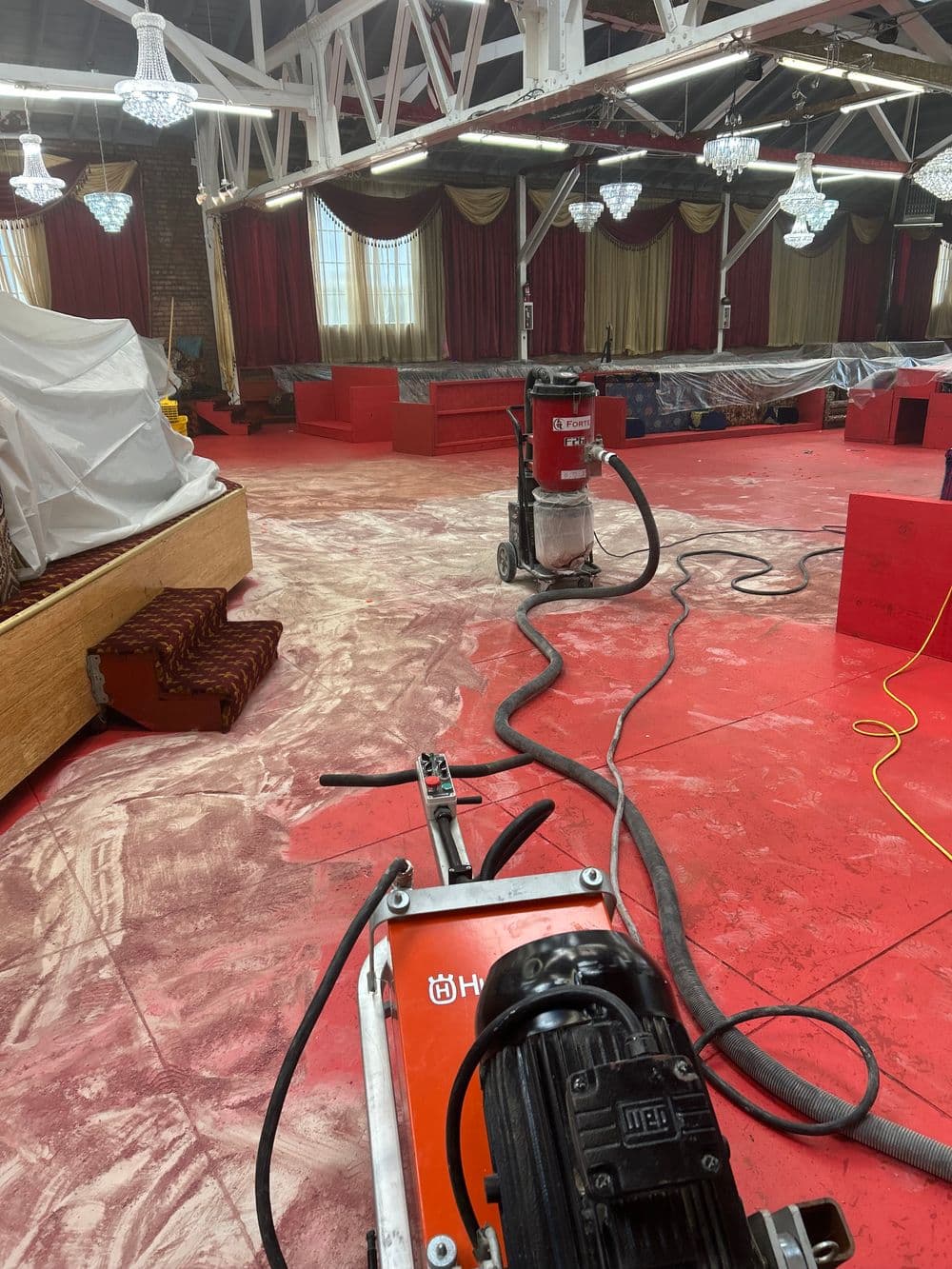 Floor preparation in progress with red surface and industrial vacuum equipment in a renovated venue.