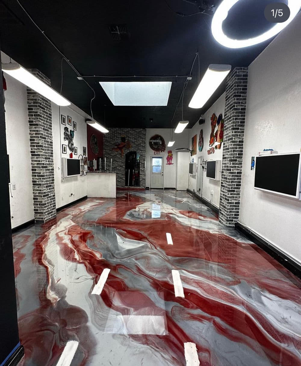 Modern art studio interior with unique red and gray epoxy flooring and black brick walls.