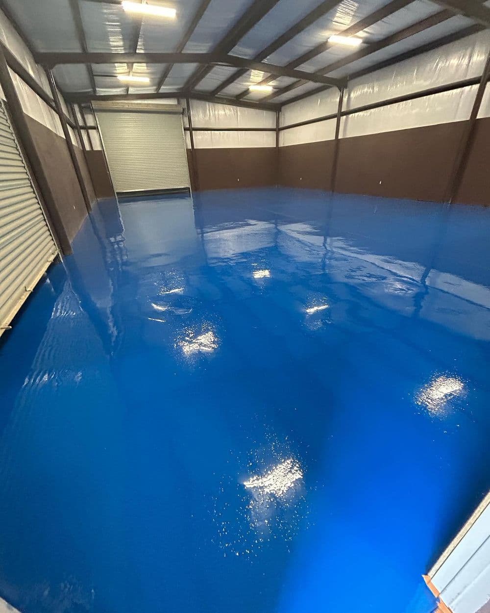Bright blue epoxy floor in a spacious industrial warehouse with metal walls.