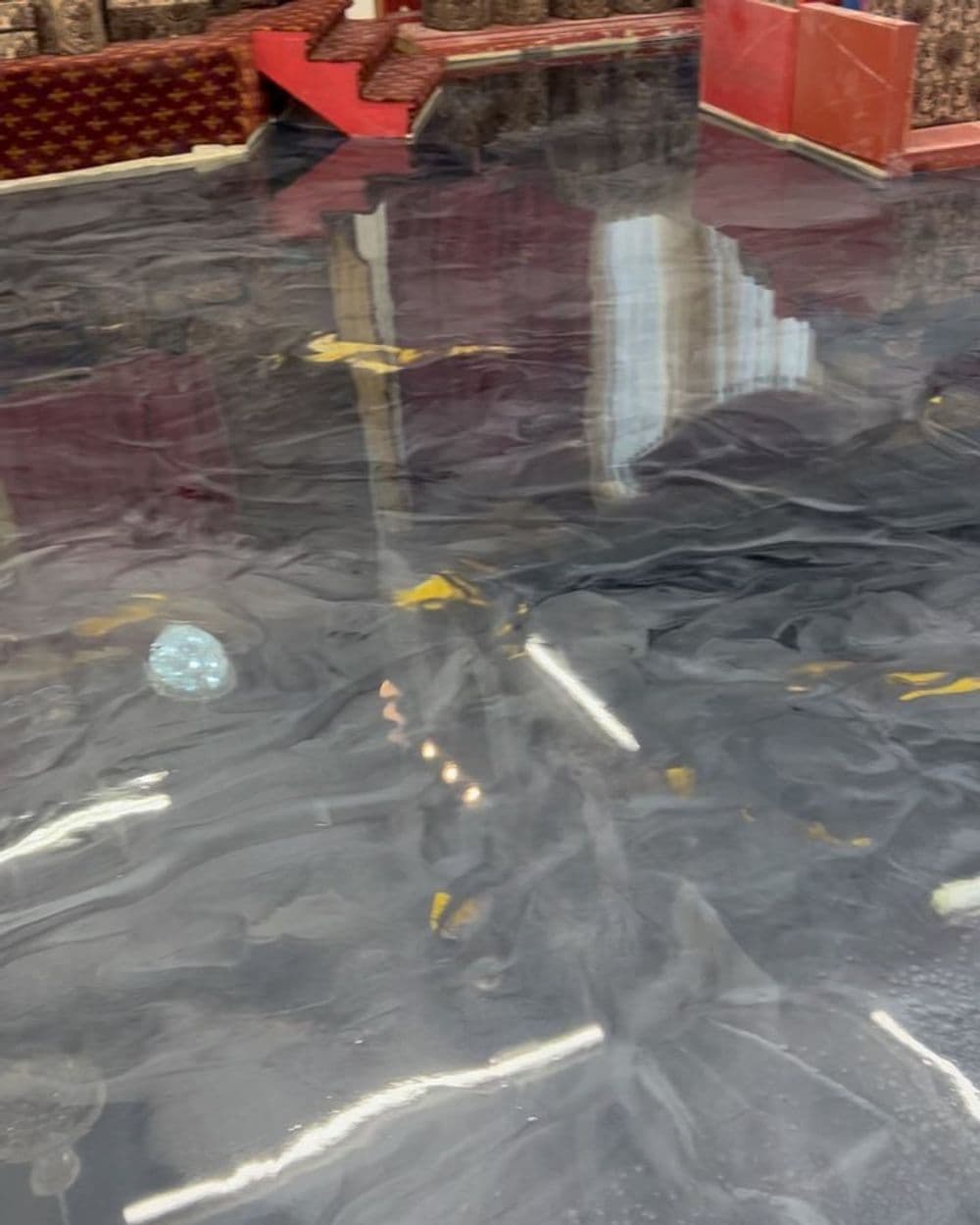 Glossy black epoxy floor with swirling patterns and reflections in a modern interior space.
