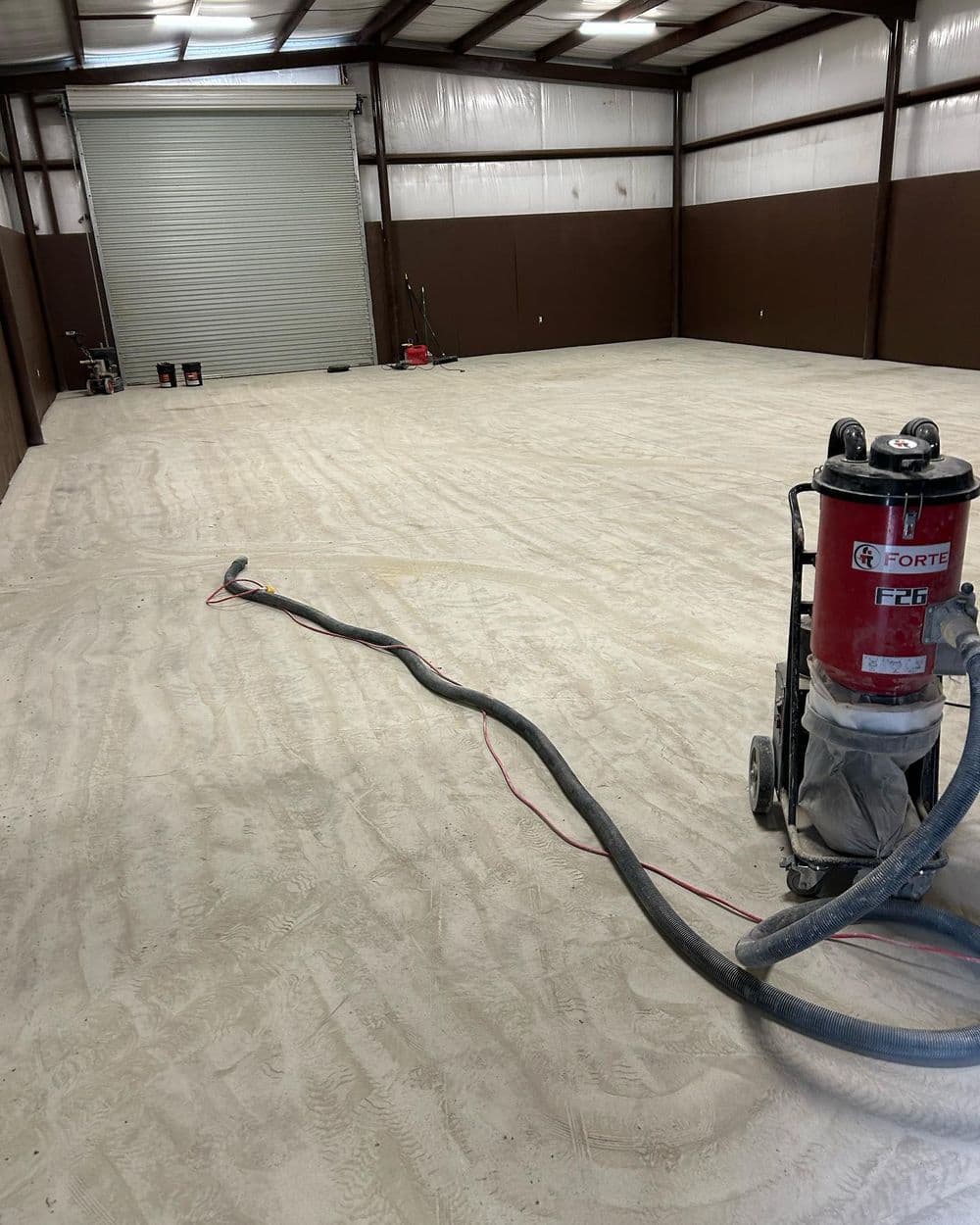 Vacuum cleaner on sandy floor in industrial warehouse space ready for renovations.