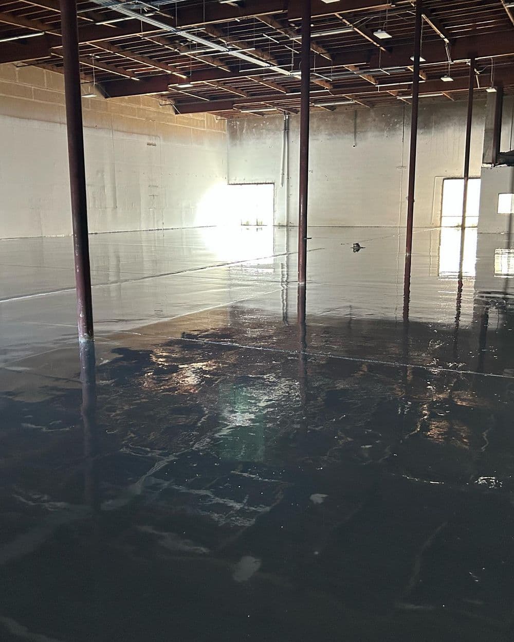 Flooded commercial space with standing water and exposed beams, reflecting light.