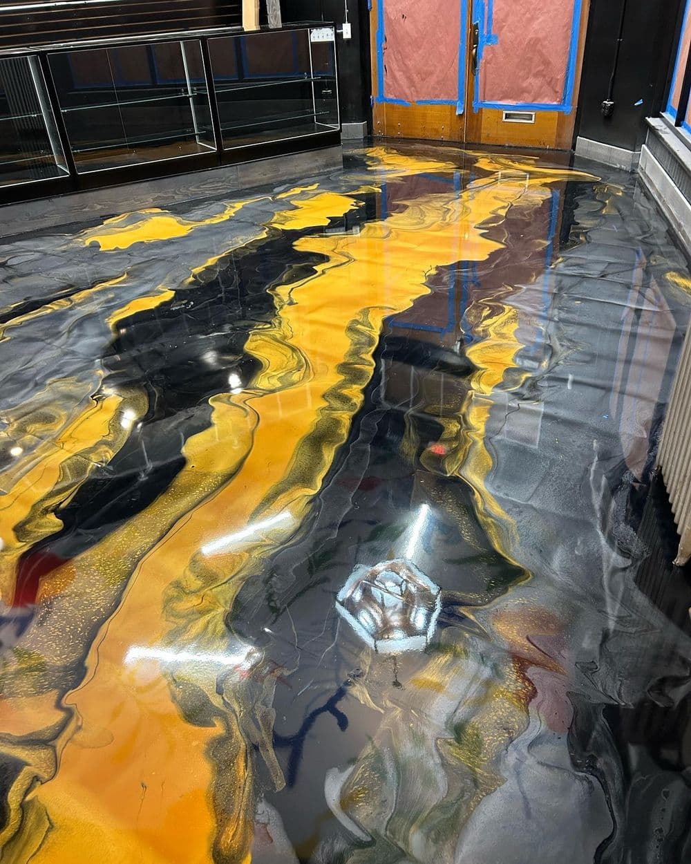 Artistic epoxy floor with swirls of black, gold, and gray in a modern interior space.