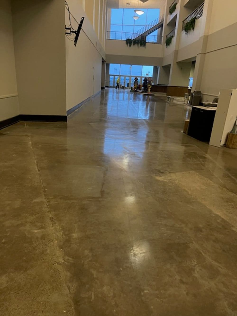 Polished concrete corridor with large windows and construction workers in the background.