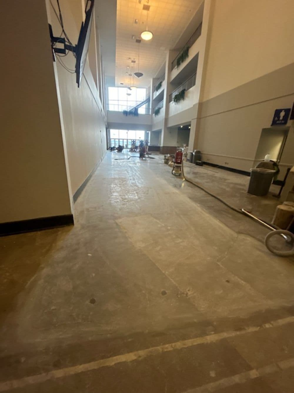 Conference center hallway under renovation with cleaning equipment and large windows.